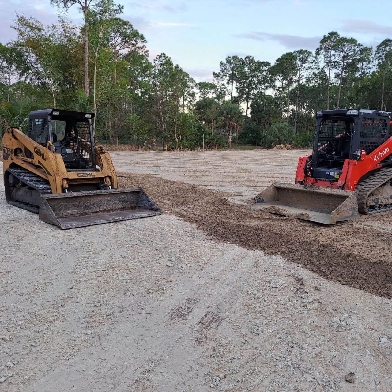 Two skid steer loaders are parked in a dirt field.
